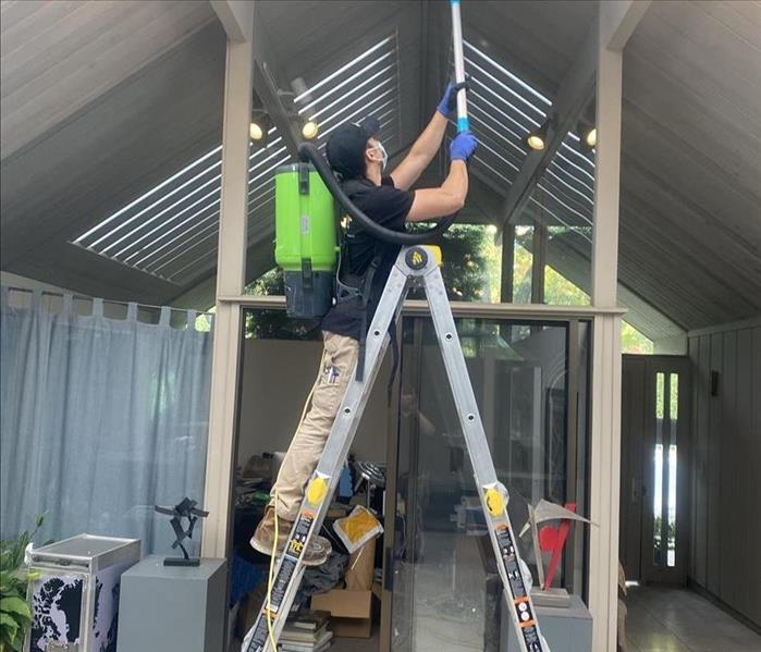 Technician on a ladder using a backpack HEPA vacuum to clean ceiling