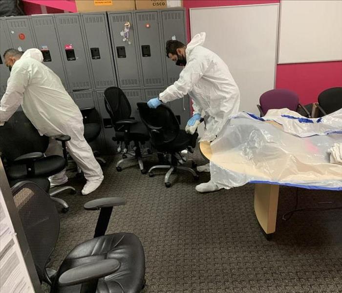 Two technicians in white tyvex suits performing deep cleaning on conference room chairs